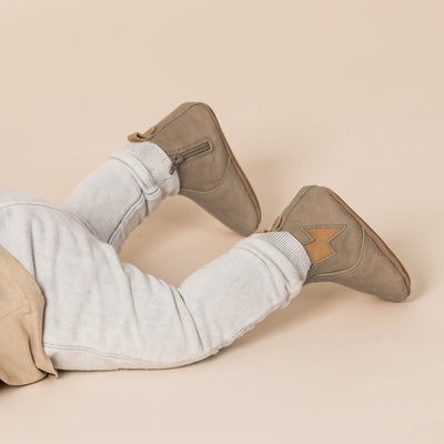 Baby on tummy wearing baby electric boots in colour taupe