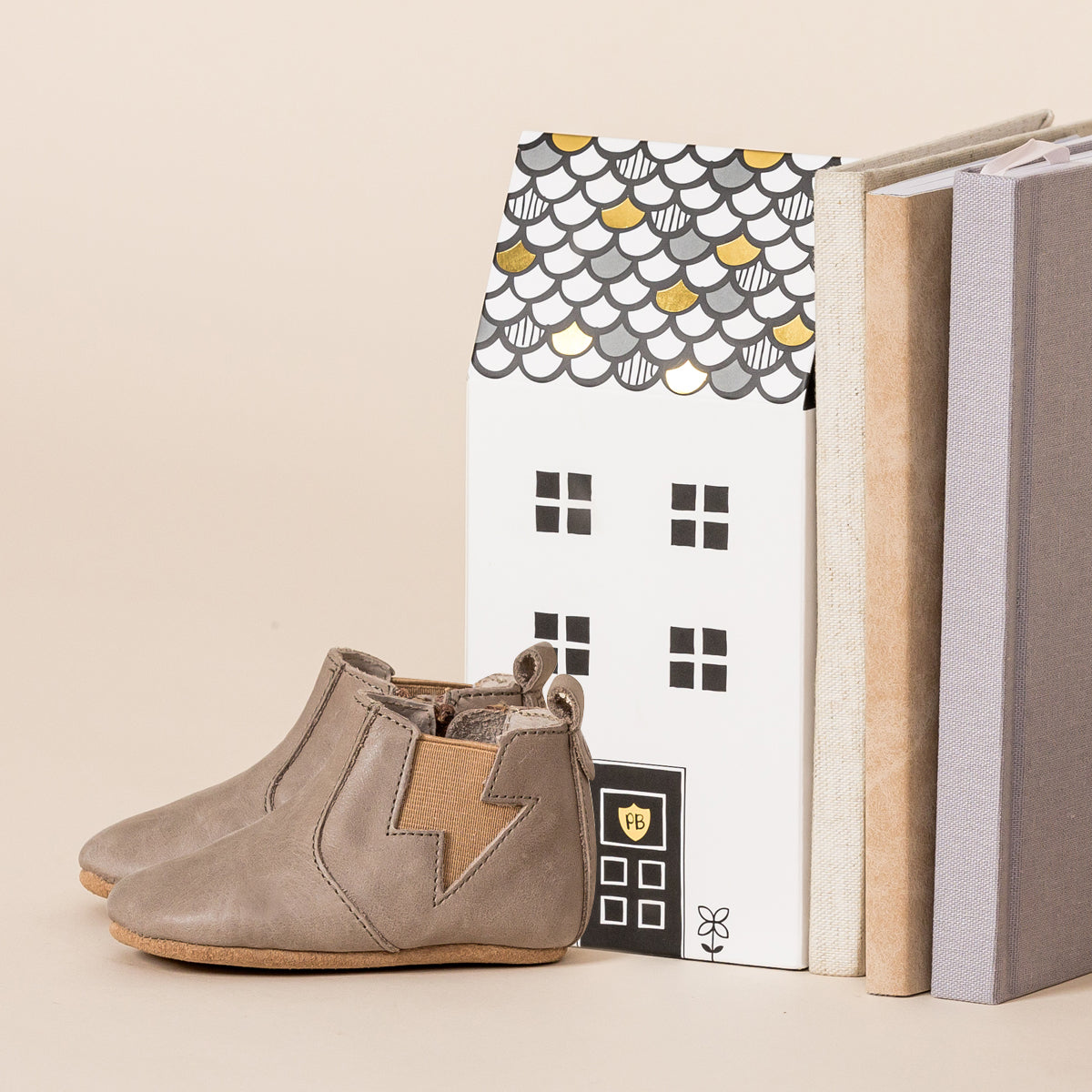 Side view of baby electric boots in colour taupe next to cardboard house