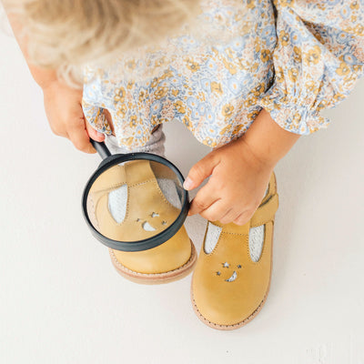Toddler holding magnifying glass over Amelia sandals in colour honey