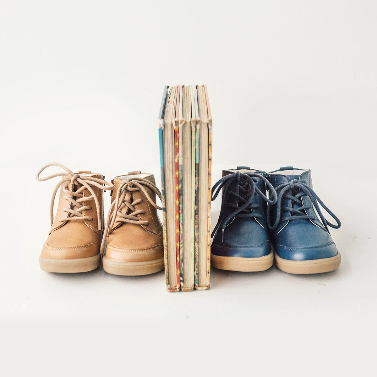 Two pairs of Archie boots next to books. Colour tan and midnight blue