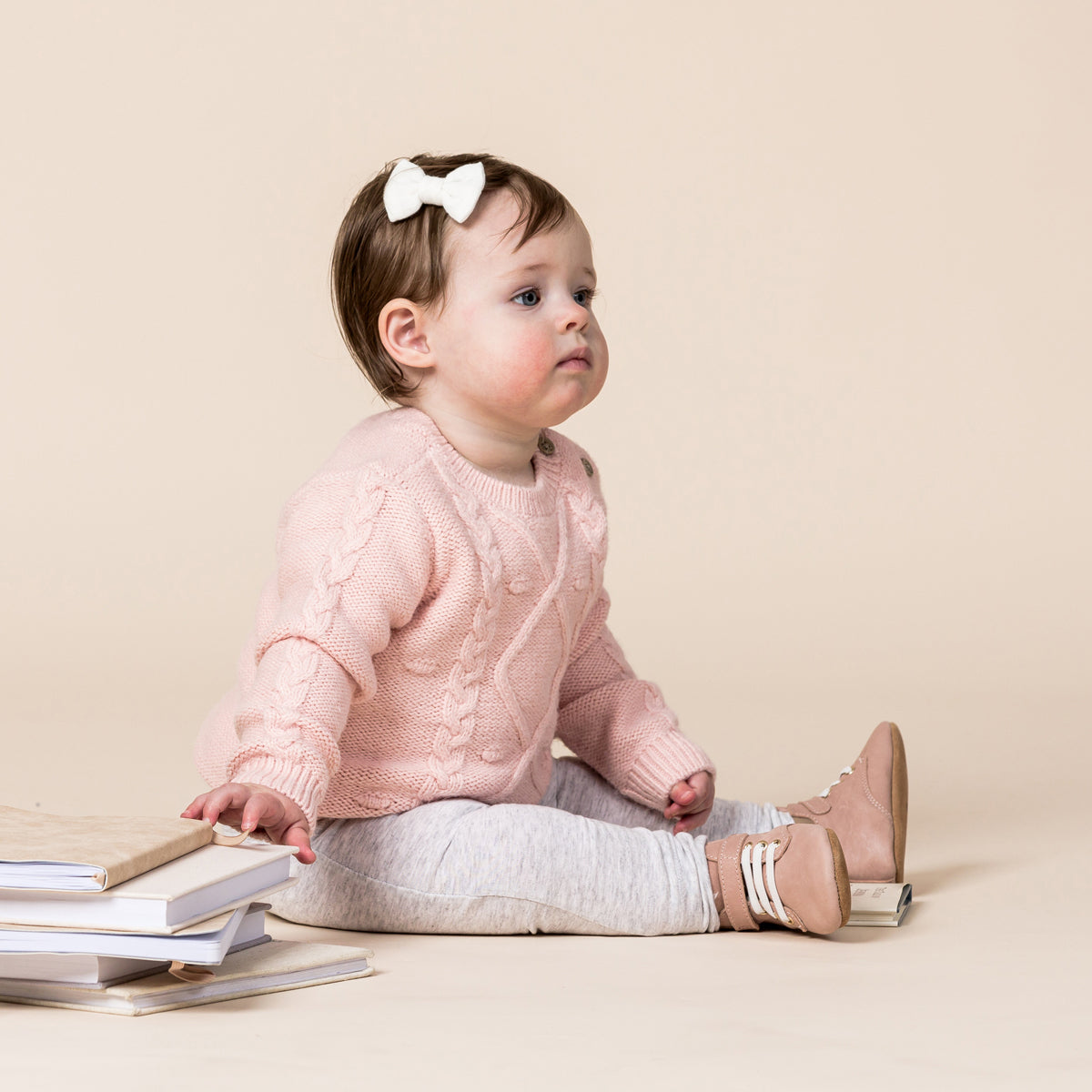 Toddler sitting on the ground wearing Archie baby boots in blush pink