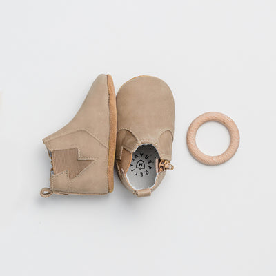 Pair of baby electric boot in colour sand next to wooden toy