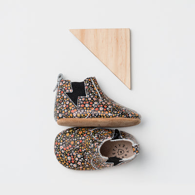 Pair of baby boots with flower design next to wooden triangle toy