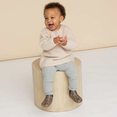 Baby laughing wearing baby boots with flower design sitting on wooden box
