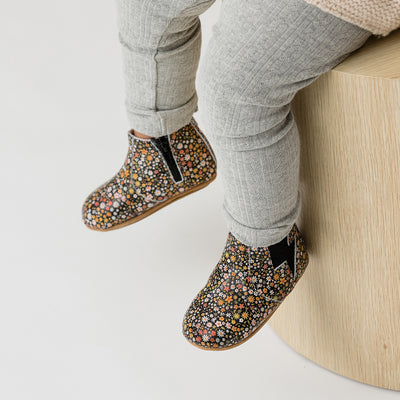Baby wearing baby boots with flower design, sitting on wooden box