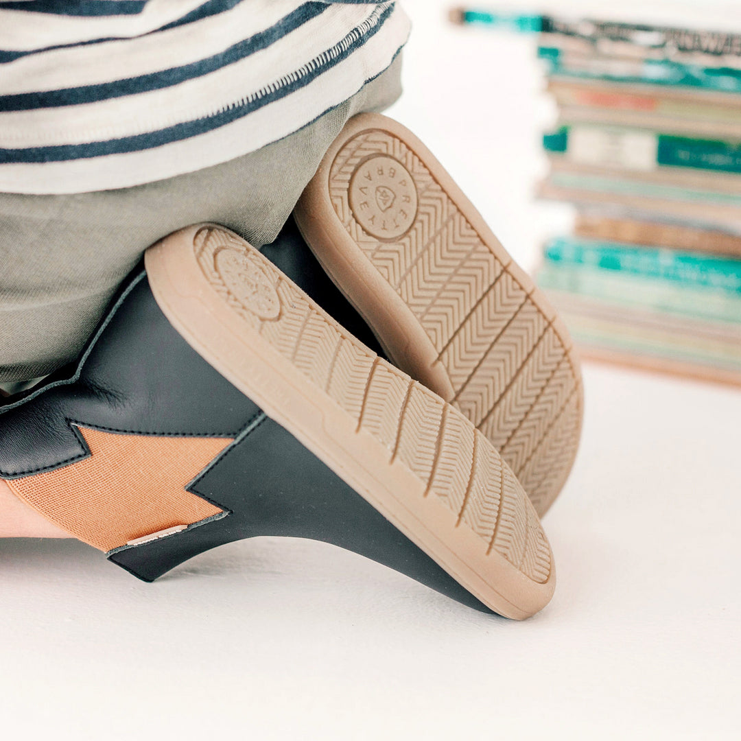 Child sitting wearing lightning detail boot in colour black.