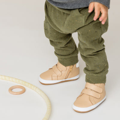 Toddler wearing green trousers and Butterfly hi-top shoe in camel