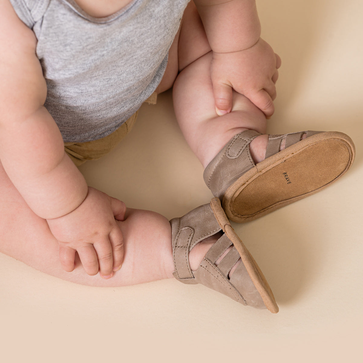 Baby sitting on the ground wearing Charlie sandal in Taupe colour